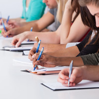 Cropped image of university students writing at desk in classroom
